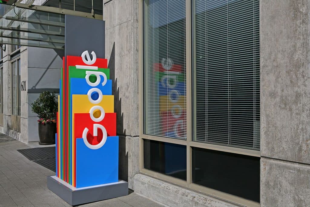 Google sign with colorful blocks stands next to a window in an urban setting.