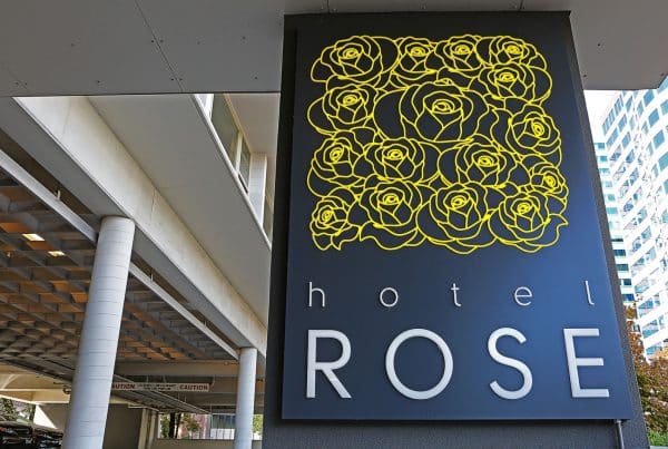 Sign for Hotel Rose featuring a black background with a pattern of yellow roses and the words "hotel ROSE" beneath. The building is visible in the background.