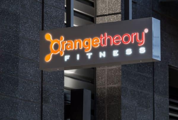A lit sign reading "Orangetheory Fitness" is mounted on a building wall.