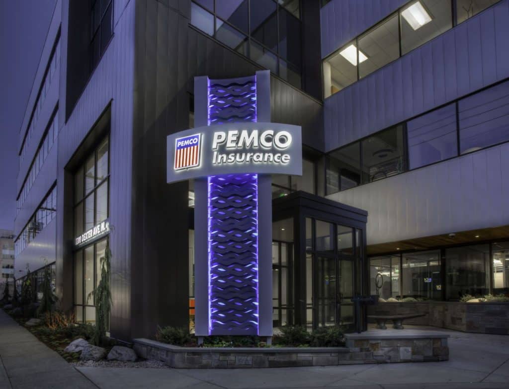 Building exterior with a PEMCO Insurance sign illuminated at night, featuring modern architecture and lit windows.