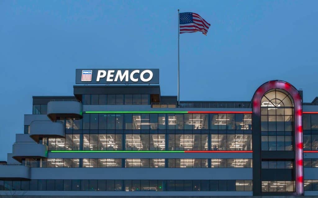Office building with "PEMCO" signage at night, featuring illuminated windows and an American flag on the roof.
