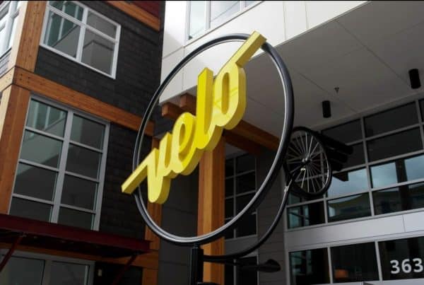 Yellow "Velo" sign with a bike wheel decor against a modern building facade.