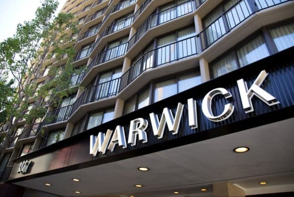 Exterior of the Warwick Hotel with large signage under a high-rise building and adjacent trees.