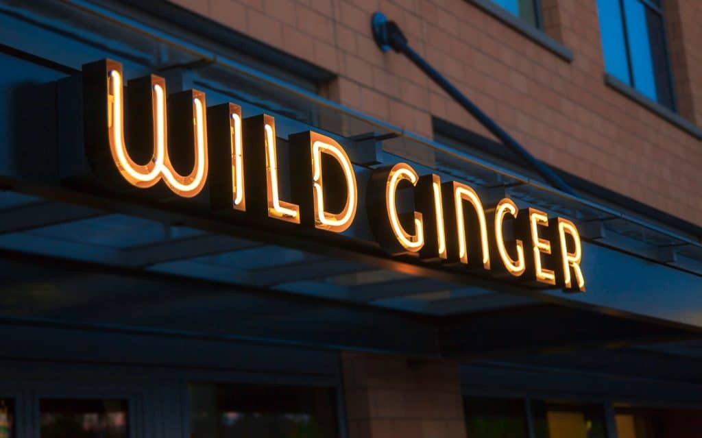 Neon sign reading "Wild Ginger" on the exterior of a brick building.