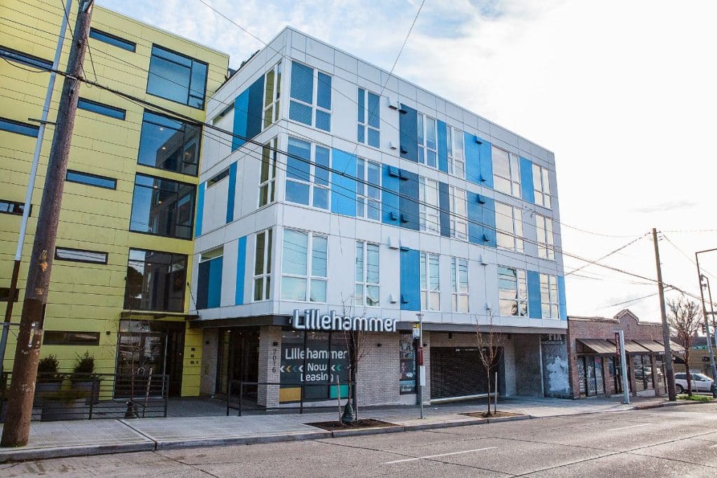 Modern building with colorful geometric panels and a sign reading "Lillehammer." It features large windows and is situated on a street corner with power lines visible.