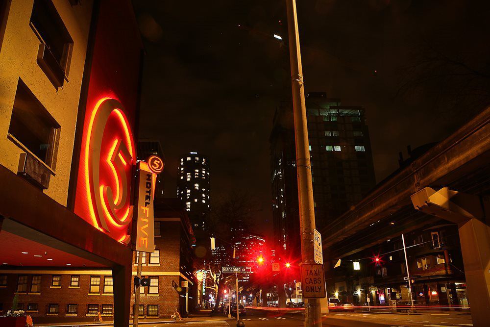 Nighttime urban scene with illuminated Hotel Five sign, city street, and high-rise buildings in the background. Traffic lights and streetlights cast a warm glow over the area. Nighttime urban scene with illuminated Hotel Five sign, city street, and high-rise buildings in the background. Traffic lights and streetlights cast a warm glow over the area.
