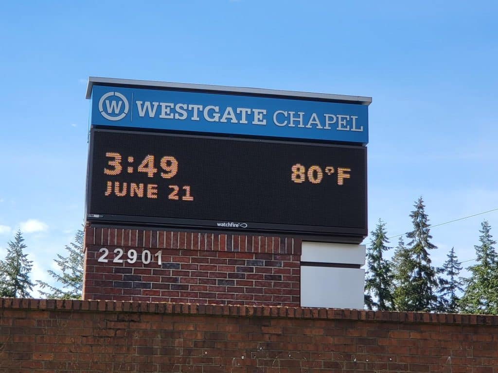 Electronic sign for Westgate Chapel displays the time 3:49, date June 21, and temperature 80°F, against a background of trees and a blue sky.