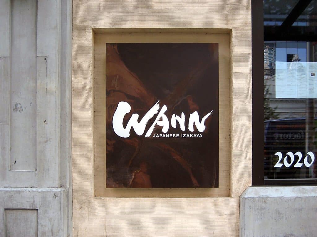 Sign reading "WANN Japanese Izakaya" on a building wall. Sign reading "WANN Japanese Izakaya" on a building wall.