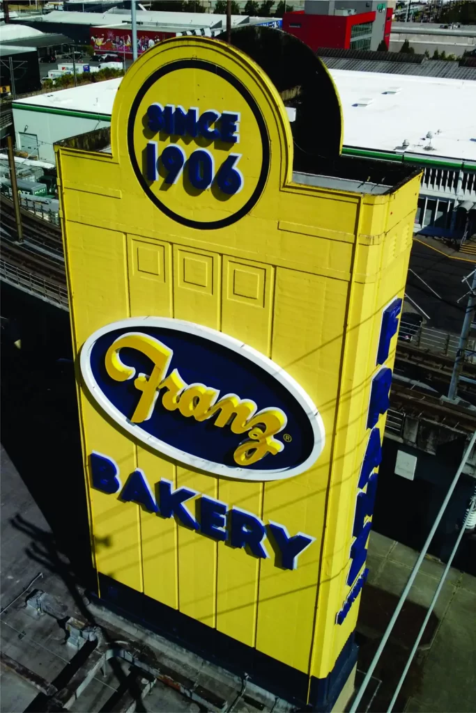 Tall yellow sign for Franz Bakery with "Since 1906" at the top, located in an urban setting.