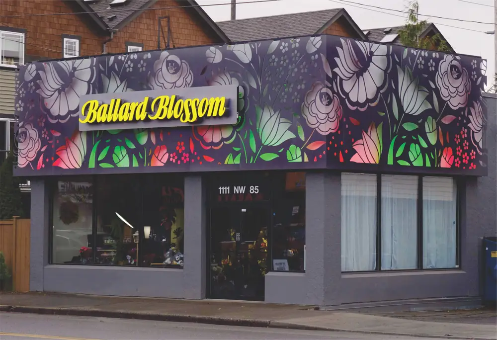 A flower shop with a colorful floral mural on the facade and the sign "Ballard Blossom" above the entrance.