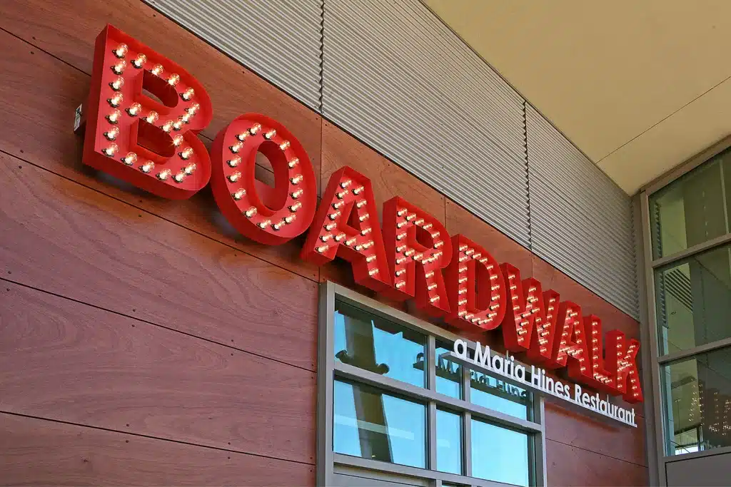 Red illuminated sign reading "BOARDWALK" on a building exterior with the text "a Maria Hines Restaurant" below it.