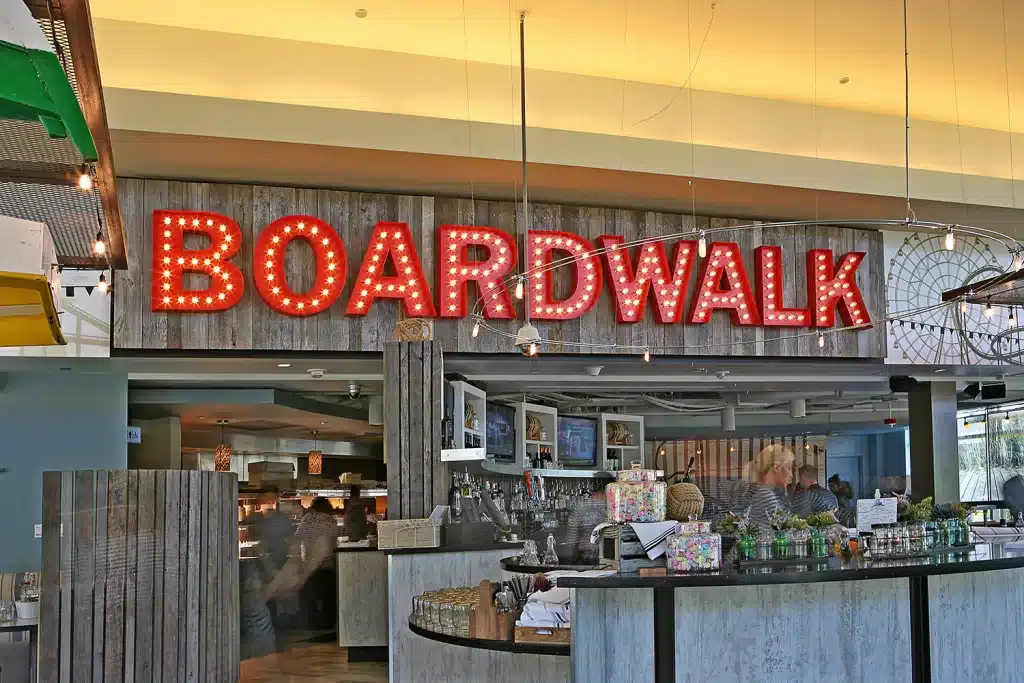 Restaurant interior with a large illuminated sign reading "BOARDWALK." The counter has various items, and staff can be seen working behind it.