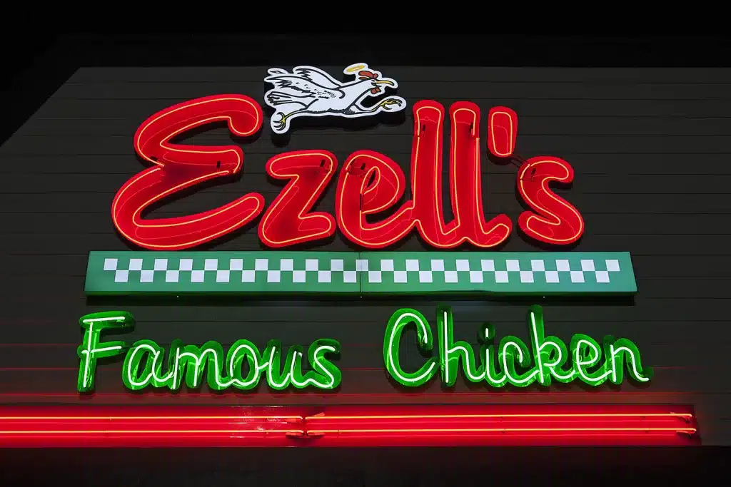 Neon sign reading "Ezell's Famous Chicken" with a flying chicken illustration.