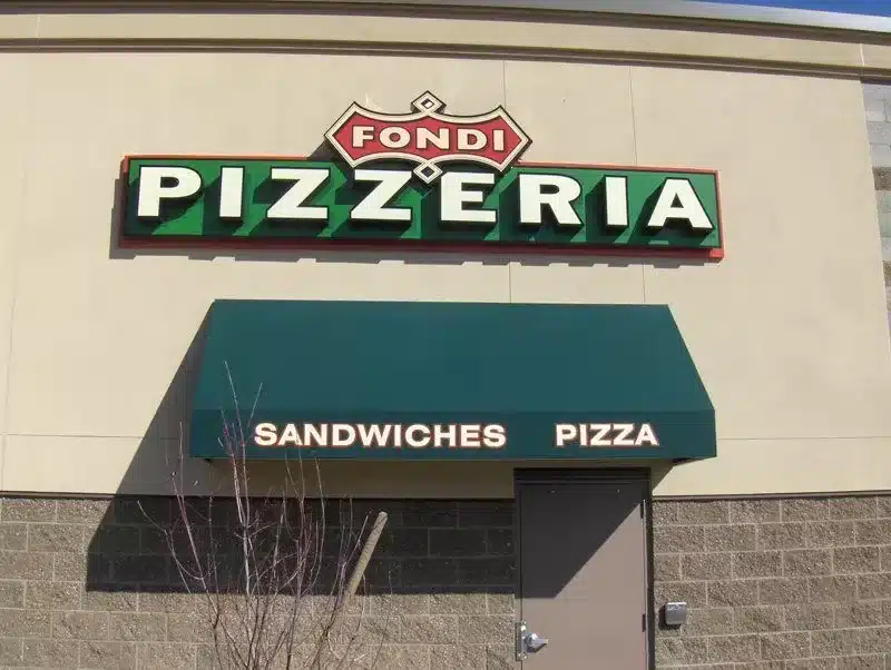 Exterior of a building with a sign reading "Fondi Pizzeria." Below it, an awning displays the words "Sandwiches" and "Pizza.