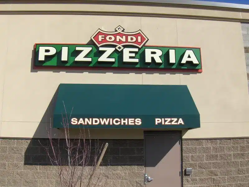 Pizzeria storefront with "Fondi Pizzeria" sign and a green awning displaying "Sandwiches Pizza.