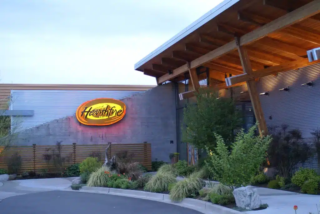 Exterior of a modern building with a neon sign displaying "Heartfire." Surrounding the building are landscaped plants and a paved driveway.