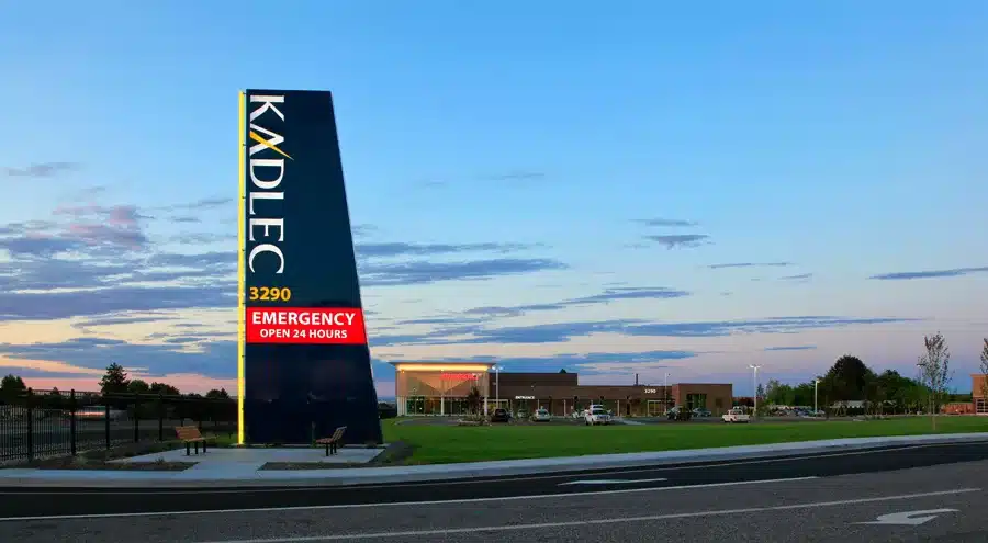 Kadlec hospital with a tall sign indicating 24-hour emergency services, set against a sunset sky.