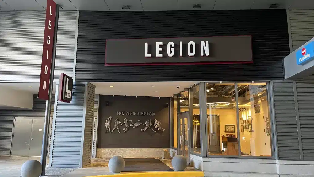 Entrance of a building with a sign reading "LEGION" above the door. A wall display inside reads "WE ARE LEGION" with human figures in various poses.
