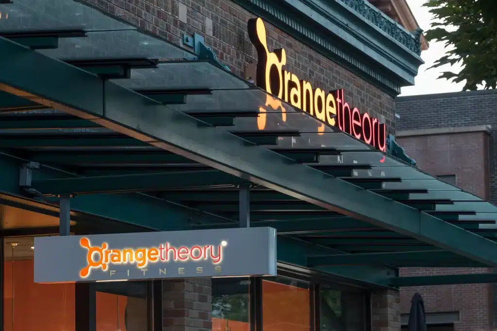 Exterior of an Orangetheory Fitness studio, featuring its logo and signage on a brick building.