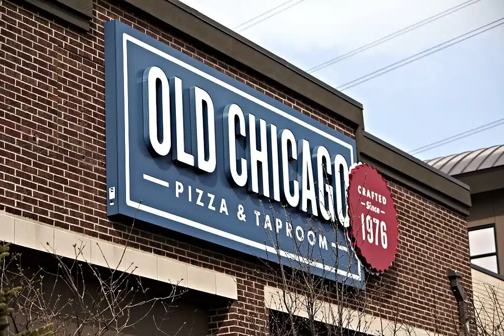 Sign for "Old Chicago Pizza & Taproom" on a brick building, featuring a red label stating "Crafted Since 1976.