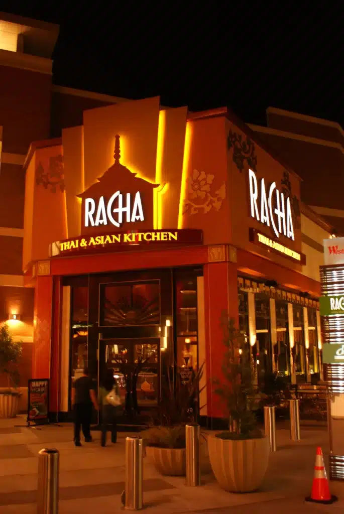 Nighttime photo of Racha Thai & Asian Kitchen, with illuminated signage and an entrance.