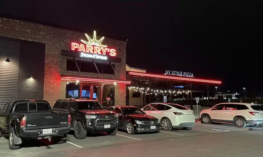 Exterior of Parry's Pizzeria at night with neon signs lit and several cars parked in front.